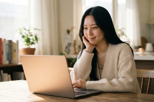 노트북 앞에서 미소 지으며 글을 쓰는 여성. 글이 안 써질 때 완벽주의를 내려놓고 초고를 작성하는 모습.